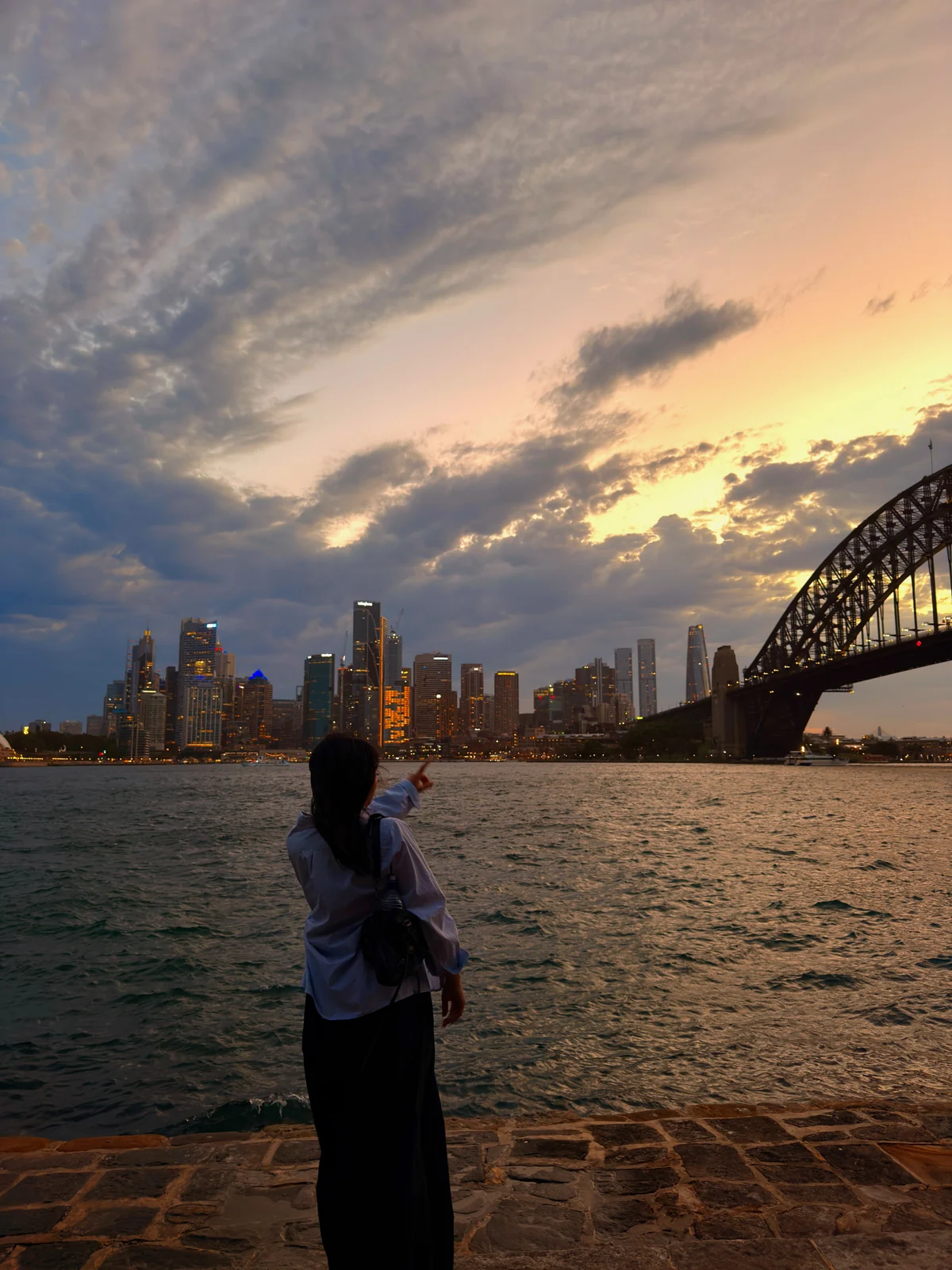 Natasha pointing at the Sydney skyline and Harbour Bridge at dusk